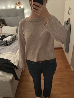 Beige stickad tröja från 157 - Mysig beige stickad tröja från 157 med avslappnad passform och långa ärmar. Tröjan har en enkel, klassisk design med ribbad halsringning och är perfekt för lager på lager under kyliga dagar.