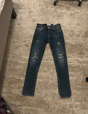 Replay Grover blå straight jeans 27/32 - Säljer ett par Replay Grover jeans i blå tvätt med straight fit. Jeansen har slitna detaljer framtill för en cool look och klassiska fem fickor. Tillverkade i jeansmaterial och har snygga kontrastsömmar. Perfekta för dig som gillar en avslappnad men ändå stilren vibe.