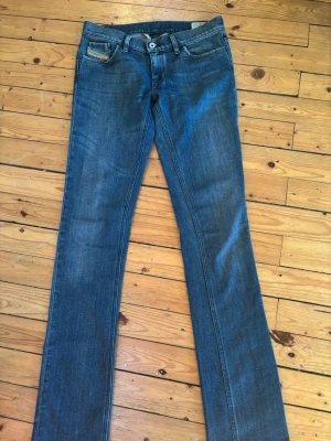 Blå Diesel LIV jeans W30 L34 - Säljer ett par klassiska blå lågmidjade jeans från Diesel, modell LIV. Jeansen har raka ben, fem fickor och snygga detaljer med Diesel Industry-märke på myntfickan. Tillverkade i slitstarkt denim med normal passform och midja.