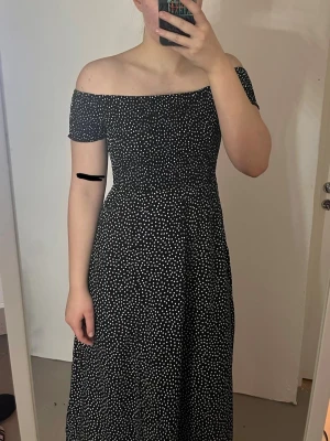 Svart offshoulder prickig långklänning - Supersnygg svart långklänning med vita prickar och offshoulder-modell. Väldigt lätt och lent material. Säljer pga jag tycker den är lite kort på mig tyvärr, jag är 172 cm. 