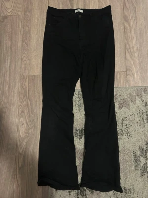 Svarta högmidjade jeans  - Säljer ett par svarta högmidjade jeans från Gina tricot storlek L. Jeansen har klassisk framficksdesign, knapp och dragkedja framtill samt utsvängda ben. Materialet är mjukt och stretchigt för extra komfort.