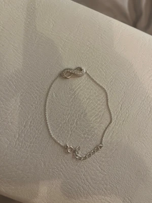 Silverarmband med evighetssymbol - Säljer ett tunt och stilrent armband i äkta silver (925) med en glittrig evighetssymbol dekorerad med små stenar. Kedjan är justerbar och har en enkel låsning. Perfekt för dig som gillar minimalistiska smycken med en touch av bling. Kedjans längd: 17cm + 3cm. Aldrig använt.