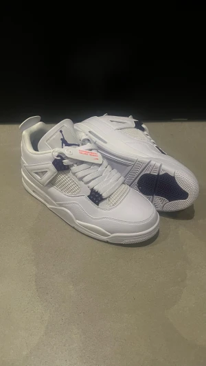 Nike Air Jordan 4 vit/lila sneakers - Nike Air Jordan 4 sneakers i vitt skinn med lila detaljer och meshpaneler. Klassisk siluett med snörning, rund tå och synlig Air-sula. Jumpman-logga på plös och häl. Perfekta för dig som vill ha en clean och sportig look.