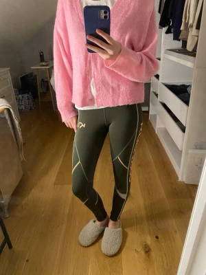 Kari Traa gröna tights - Säljer ett par gröna tights från Kari Traa med snygga kontrastsömmar och orange logga längs benet. De har dragkedja vid benslut och reflexer. Perfekta för träning eller chill dagar.