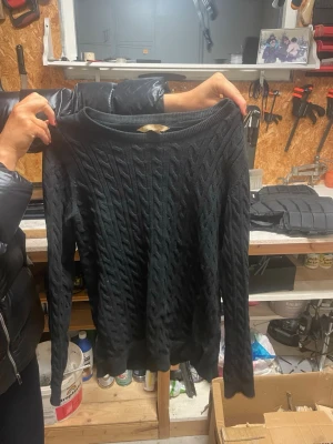 Svart kabelstickad tröja Basic U - Kabelstickad svart tröja från Basic U collection i storlek S. Tröjan har rund halsringning och långa ärmar. Perfekt för dig som gillar klassisk stil med en twist. Materialet känns mjukt och passar till både jeans och kjol.