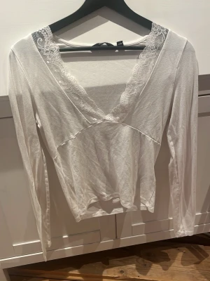 Vit spetsdetaljerad blus Vero Moda - Säljer en vit långärmad blus från Vero Moda med v-ringning och fina spetsdetaljer längs urringningen. Perfekt för dig som gillar en feminin och enkel stil. Snygg att matcha med både jeans och kjol. Supermjuk och härlig att ha på sig!! Säljer för att den tyvärr inte kommer till användning.