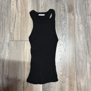 Svart ribbad linnetopp från Zara - Säljer en svart ribbad linnetopp från Zara Trafaluc. Toppen är ärmlös med breda axelband och har en tight passform. Perfekt till sommarens alla outfits och enkel att styla med olika accessoarer.