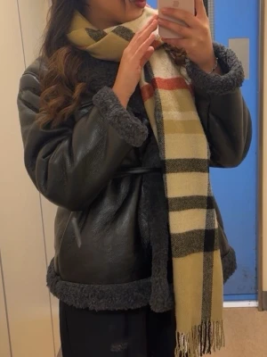 Svart teddyjacka med bälte - Säljer en svart teddyjacka med bred krage och mysigt foder. Jackan har ett bälte i midjan som ger en snygg siluett och detaljer i teddy längs krage, ärmslut och nederkant. Perfekt för kalla dagar och riktigt trendig look. ((Går och pruta ner!))