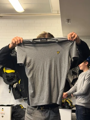 Grå t-shirt från Lyle & Scott - Säljer en stilren grå t-shirt från Lyle & Scott med klassisk gul logga på bröstet. T-shirten är kortärmad och har en normal passform. Perfekt för dig som gillar enkel och snygg stil.