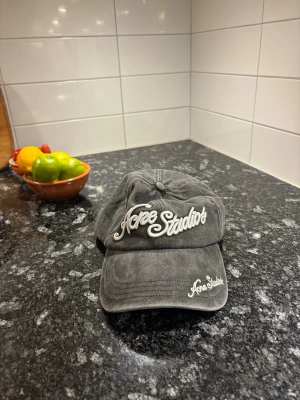 Grå Acne Studios keps i bomull - Säljer en grå keps från Acne Studios med broderad logga framtill och på skärmen. Kepsen är tillverkad i 100% bomull och har en klassisk, avslappnad passform. Perfekt accessoar för en cool och enkel stil.