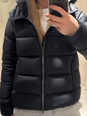 Svart pufferjacka från Colmar - Nypris: 6 999kr på SkiStar. Säljer min svarta glansiga pufferjacka från Colmar med huva och tydlig logga på ärmen. Jackan har inga defekter och är vadderad för extra värme. Perfekt för kalla dagar och har en clean, glansig look som passar till allt. Säljer den pga för lite användning. Köptes januari 2025 på SkiStar. 
