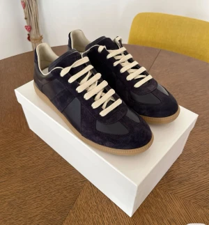 Maison Margiela sneakers i mocka och skinn - Snygga sneakers från Maison Margiela med mörkblå och grå paneler i mocka och skinn, beige snörning och klassisk gummisula. Modellen har rund tå och platt sula, perfekt för dig som gillar stilrena och exklusiva sneakers med retrovibe. Väldigt osäker på äktehet, därav det billiga priset. 