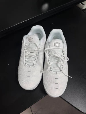 Helt ny Nike Air Max Plus vita sneakers - Nike Air Max Plus sneakers i helvitt med grå detaljer på sulan och gula inslag i luftkudden. Skorna har snörning, mesh och syntetmaterial på ovandelen samt Tn-logga bak. Snygg, sportig design med platt sula och rund tå. Perfekt för dig som gillar klassiska och cleana sneakers.