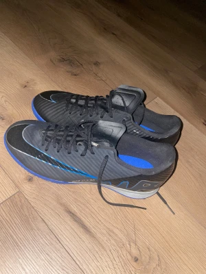 Nike fotbollsskor svart/blå - Säljer ett par svarta Nike fotbollsskor med blå. Skorna har snörning och en rund tå, med en snygg Nike-logga på sidan och framtill.  . Perfekt för dig som vill ha stil på planen.   Hej de är helt nya har inte använt någon gång de är storlek 42-43 kostade 1200