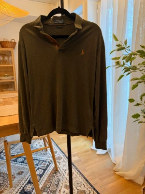 Mörkgrön pikétröja från Polo Ralph Lauren - Snygg mörkgrön långärmad pikétröja från Polo Ralph Lauren med klassisk krage och knappslå. Slim fit-modell med broderad logga på bröstet. Perfekt för dig som gillar stilrena och tidlösa plagg.