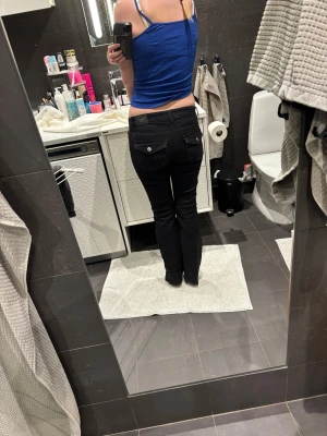 Svarta bootcut jeans med fickdetaljer - Snygga svarta jeans från Gina Tricot med bootcut och låg midja. Klassisk femficksmodell fram och bakfickor med lock och silverknappar. Jeansen har en rak passform över låren och lätt utsvängda ben. Perfekta för dig som gillar stilrena och coola jeans.