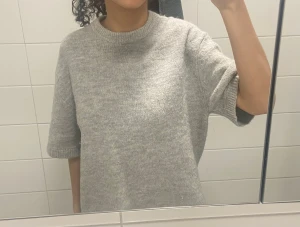 Grå stickad tröja Gina Tricot XS - Mysig grå stickad tröja från Gina Tricot i storlek XS. Tröjan har en rund halsringning och korta ärmar med ribbade muddar. Den är loose fit och har en enkel, stilren look som passar perfekt till jeans eller kjol. Materialet är mjukt och känns skönt mot huden. Tröjan har ett litet hål på baksidan. 