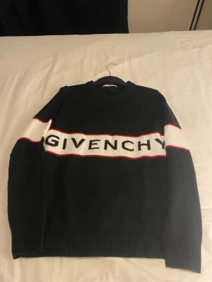 Svart stickad tröja från Givenchy - Svart stickad tröja från Givenchy med vit panel och röd kant över bröstet där loggan är broderad i svart. Tröjan har rund hals, ribbade muddar och lång ärm. Snygg och stilren design som sticker ut med den breda loggan.