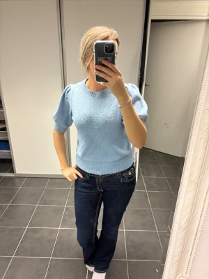 Ljusblå stickad topp med puffärm - Säljer en ljusblå stickad topp med korta puffärmar och rund hals. Toppen har ribbade muddar vid ärmslut och nederkant, vilket ger en snygg och modern siluett. Perfekt för dig som gillar en enkel men trendig look.