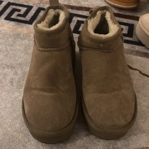 Beige mockaboots med foder - Säljer ett par beige boots i mocka med mjukt, ljust foder på insidan. Skorna har rund tå, platt sula och en låg siluett som slutar vid ankeln. Perfekta för kalla dagar när du vill ha både stil och komfort.