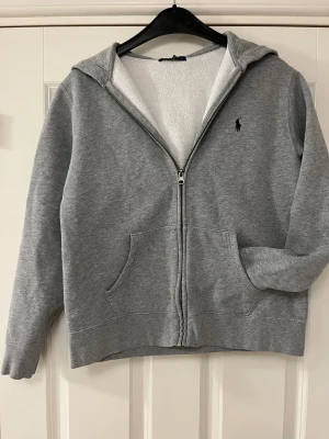 Grå hoodie från Polo Ralph Lauren - Riktigt snygg grå hoodie från Polo Ralph Lauren med dragkedja i storlek L (14-16)