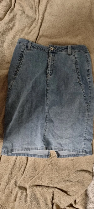 Ljusblå jeanskjol från Mingel - Snygg ljusblå jeanskjol från Mingel med klassisk rak passform och slits både fram och bak. Kjolen har hällor för bälte, fickor fram samt knapp och dragkedja i midjan. Perfekt för dig som gillar enkel denimstil.