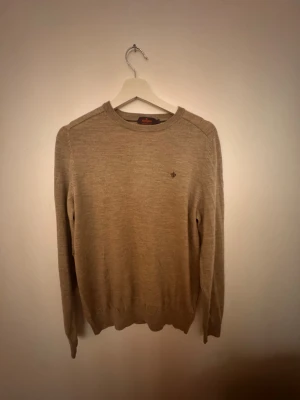 Beige merinoulltröja från Morris - Snygg beige stickad tröja från Morris i 100% merinoull och Kashmir. Klassisk rund hals och diskret Morris-logga broderad på bröstet. Tröjan har långärmade ribbade muddar och en clean, stilren look som funkar till allt.