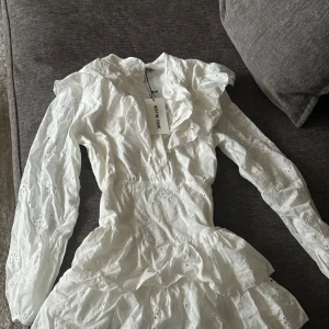 Studentklänning - Supersöt vit kort studentklänning med volanger och broderade detaljer från Meet The There. Klänningen är storlek M/L men den passar en s, MAX liten M. Den har tunna shorts i kjolen och midjan är töjningsbar. Aldrig använd. Nypris när jag köpte 850kr.