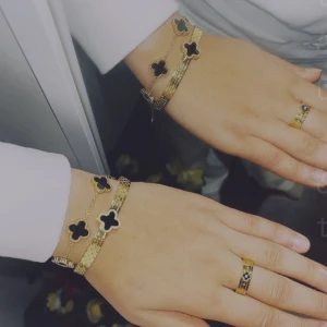 Två vattentåliga Guldarmband och ring med svart klöver  - Snyggt guldarmband med svarta klöverformade detaljer och matchande ring. Armbandet har en tunn kedja och dekorativa klöverhängen, medan ringen har en svart klöver i mitten. Perfekt för dig som gillar unika smycken med gulddetaljer. Och  vattentåliga smycken