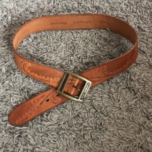 Brunt skärp i skinn med mönster - Snyggt brunt bälte i skinn med ingraverat mönster och en fyrkantig metallspänne. Perfekt accessoar för att lyfta din outfit med en western-vibe🤠