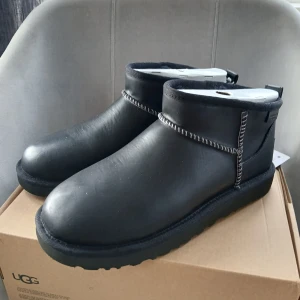 Nya UGG Classic Ultra Mini bootsstrl 39 - Svarta UGG Classic Ultra Mini boots i skinn med låg siluett och synliga kontrastsömmar. Skorna har rund tå, platt sula och dragflik bak. Perfekta för dig som vill ha en clean och stilren look med maximal komfort.