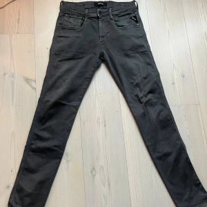 Replay Anbass Hyperflex grå jeans - Säljer ett par grå Replay Anbass Hyperflex jeans med klassisk femficksdesign och smal passform. Jeansen har stretchigt material för extra komfort och snygg Replay-detalj vid fickan. Perfekta för dig som gillar stilrena och moderna jeans.