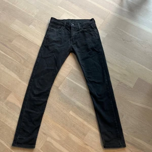 Levi's 512 svarta jeans 30/32 - Svarta Levi's 512 jeans med smal passform och klassisk femficksdesign. Jeansen har normal midja och raka ben med en lätt stretchig känsla. Perfekta för dig som gillar en stilren och enkel look. Materialet är mjukt och följsamt jeans.