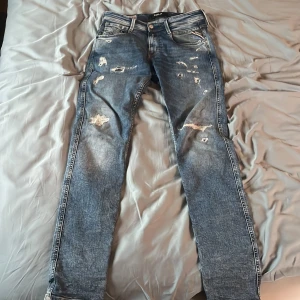 Replay blå slitna jeans, midja 28/32 - Blå jeans från Replay med slitna detaljer och hål för en cool, avslappnad look. Tillverkade i ekologisk bomull och har klassisk femficksdesign. Jeansen har normal passform och raka ben, perfekt för dig som gillar streetstyle. Nypris 1599