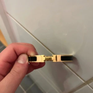 Svart och guld armband  - Snyggt armband  i guldtonat metall med svarta detaljer och klassiskt H-spänne. Stilren och  design som verkligen sticker ut på handleden. Perfekt accessoar för dig som gillar exklusiva smycken och vill ha något som känns både trendigt och tidlöst.
