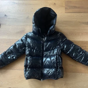 Svart pufferjacka från Colmar - Säljer en svart, glansig pufferjacka från Colmar med huva och dragkedja framtill. Jackan har ett coolt, quiltat mönster och logotyp på ärmen. Perfekt för dig som vill ha en varm och snygg look under vintern. Köpt från kidsbrandstore för 5000. Men tyvärr har den blivit lite liten. Jag är 170 o den är lite kort i armarna på mig. Passar dig som vill ha en glansig, varm och skön jacka🥰