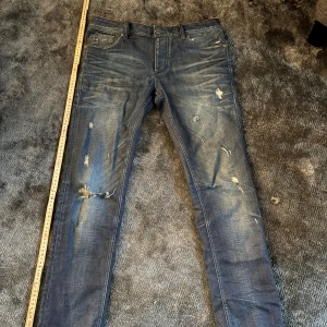 Blå slitna jeans från Jack & Jones - Säljer ett par blå jeans från Jack & Jones Originals med snygga slitningar och distressed detaljer. Jeansen har klassisk femficksdesign, normal midja och raka ben. Materialet är jeans i bomull och de har en cool, använd look som passar perfekt till streetwear. Pris kan diskuteras🙌🏻