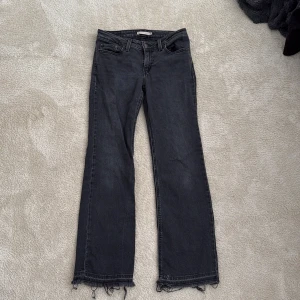 Levi's svarta bootcut jeans low waist - Svarta Levi's jeans i bootcut-modell med låg midja. Jeansen har klassiska fem fickor, råa och fransiga benslut samt tydliga sömmar. Materialet är jeans i bomull och passformen är normal. Perfekta för dig som gillar en avslappnad och trendig look. Dem är välanvända och väldigt urtvättade då färgen egentligen ska va helt svart 