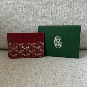Goyardd plånbok  - Supersnygg röd plånbok. Med deras ikoniska grafiska mönster. Slimmad design med flera kortfack och detaljer i skinn. Perfekt för dig som vill ha något stilrent och lyxigt i fickan.