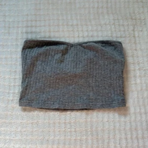 Grå ribbad tubtopp från SHEIN XS - Snygg grå tubtopp från SHEIN i storlek XS. Toppen är ribbad och har en enkel bandeau-form som sitter skönt och stilrent. Perfekt att matcha med jeans eller kjol för en chill look. Materialet är mjukt och stretchigt, vilket gör den bekväm att bära hela dagen.
