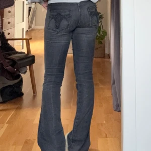 Mörkgrå bootcut jeans med detaljer på bakfickan  - Snygga mörkgrå jeans med bootcut passform och broderade detaljer på bakfickorna. Jeansen har låg midja och är tillverkade i stretchigt denim för en bekväm känsla. Storlek 27/32💞