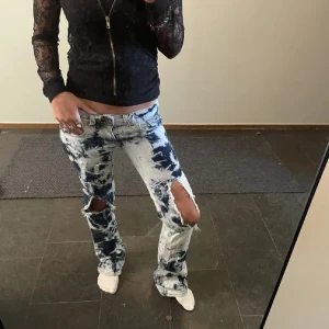 Blåvit batik jeans med slitningar - Säljer ett par unika blåvita batikmönstrade jeans med stora slitningar vid knäna. Modellen är lågmidjad och har bootcut-snitt. Perfekta för dig som vill sticka ut med en edgy och cool look🌸🌸