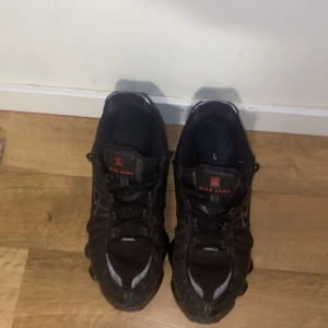 Svarta Nike Shox sneakers - Säljer ett par svarta Nike Shox sneakers med röda detaljer och silvriga inslag. Skorna har en unik fjädrande sula, snörning och meshpartier för extra ventilation. Perfekta för dig som vill sticka ut med en sportig och futuristisk look.