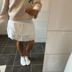 Vit volangkjol med broderade detaljer - Supersöt vit kortkjol med bred smock i midjan och två lager volanger. Kjolen har broderade blommor och spetskant längs nederdelen för extra gullig vibe. Perfekt att styla med en stickad tröja eller en enkel topp. Materialet känns som bomull och är lätt och luftigt. Kjolen är helt ny, aldrig använd!💞