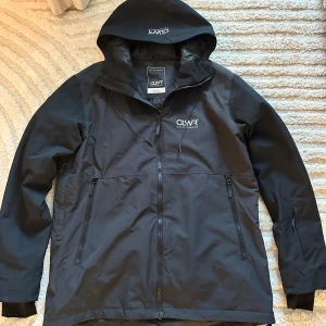 Svart skidjacka från CLWR med huva - Säljer nu en väl omhändertagen skidjacka från Colourwear med flertal praktiska fickor och spännen för att dra åt jackan. Inga defekter eller liknande. Nypris ca 1500kr längd: 80cm bredd: 65cm 