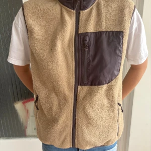 Beige fleeceväst från McKinley - Beige fleeceväst från McKinley med bruna detaljer och dragkedja framtill. Västen har en stor bröstficka i brunt tyg med dragkedja och två sidofickor. Perfekt för lager-på-lager och outdoor-vibes. Jag har storlek S i vanliga fall. 