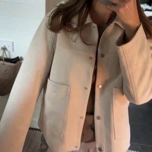 Beige tunn jacka från Stradivarius - Snygg tunn beige jacka från Stradivarius med klassisk krage, stora fickor framtill och tryckknappar. Jackan har en rak passform och är gjord i ett mjukt material som känns lite mockaliknande. Perfekt att slänga över en hoodie eller t-shirt. Endast använd några enstaka gånger, inga tecken på användning. 