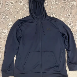 Mörkblå hoodie från Under Armour - Mörkblå hoodie från Under Armour med dragkedja och huva med snörning. Tröjan har två stora fickor framtill och är tillverkad i mjuk fleece som känns riktigt skön. Perfekt för chill dagar eller när du vill ha något bekvämt på dig. Skriv privat för fler bilder, priset kan diskuteras. Har använd några gånger annats helt ny, köpt från Zalando för 879 kr