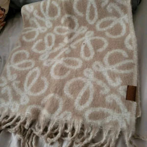 Beige och vit ullhalsduk  - Snygg beige halsduk med vitt mönster och fransar i kanterna. Tillverkad i mjuk ull som håller dig varm och stilsäker. Perfekt accessoar för att lyfta din outfit med en lyxig touch och cool design.