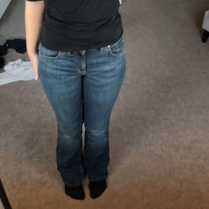 Blå bootcut jeans från Zara, stl 34 - Säljer ett par klassiska blå jeans från Zara i storlek 34. Jeansen har bootcut-modell med låg midja och raka ben som blir lite vidare nertill. Tillverkade i mjukt denimtyg med snygga detaljer och fickor både fram och bak.